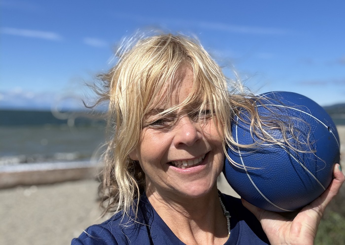 Helmy on the beach with a medicine ball on her shoulder, laughing in the wind